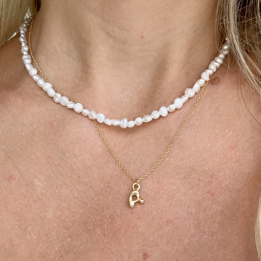 Dainty Gold puffy initial "A" pendant necklace on an 18-inch gold filled chain as seen on a model with a pearl necklace layered.