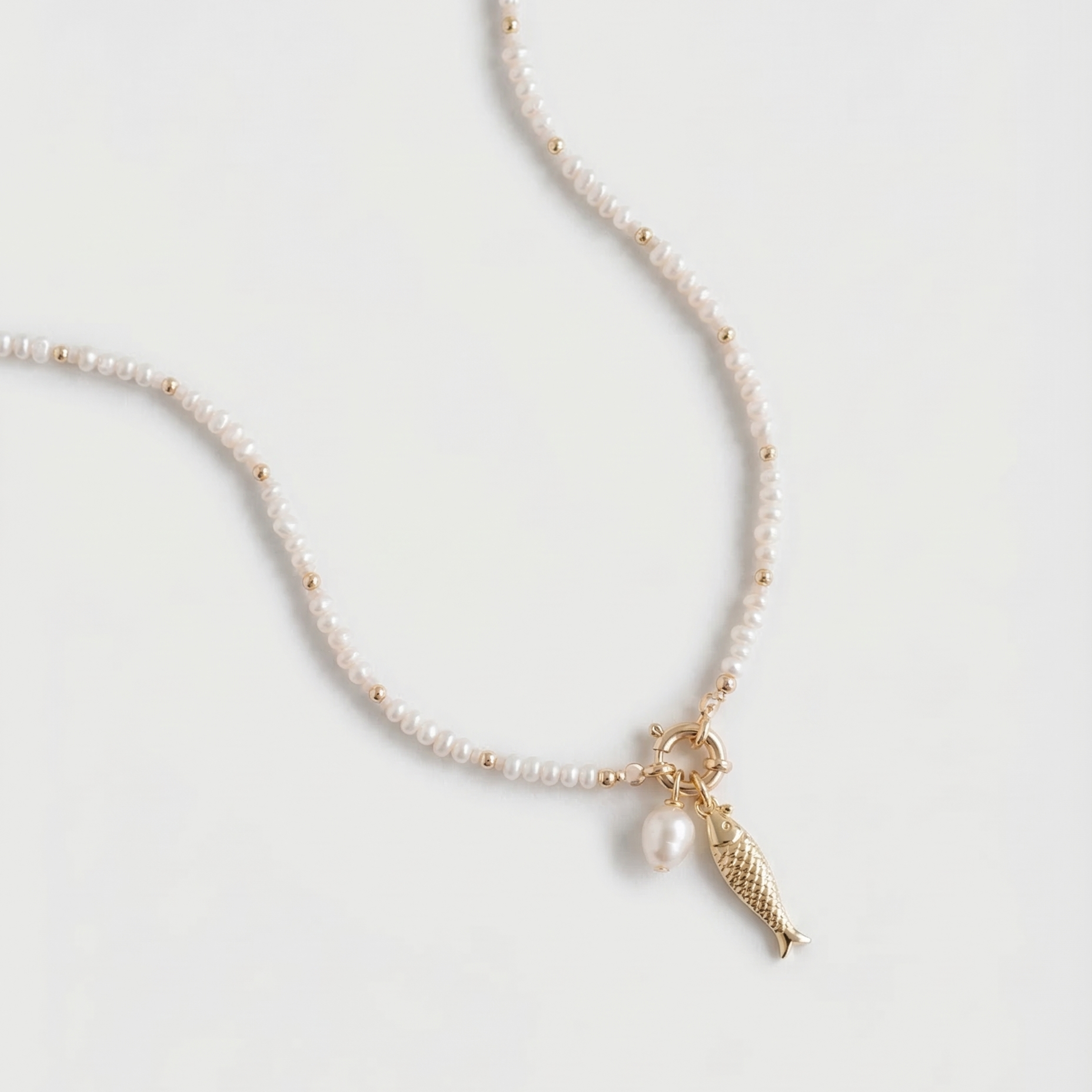 Pearl necklace with a gold fish charm on a light gray background