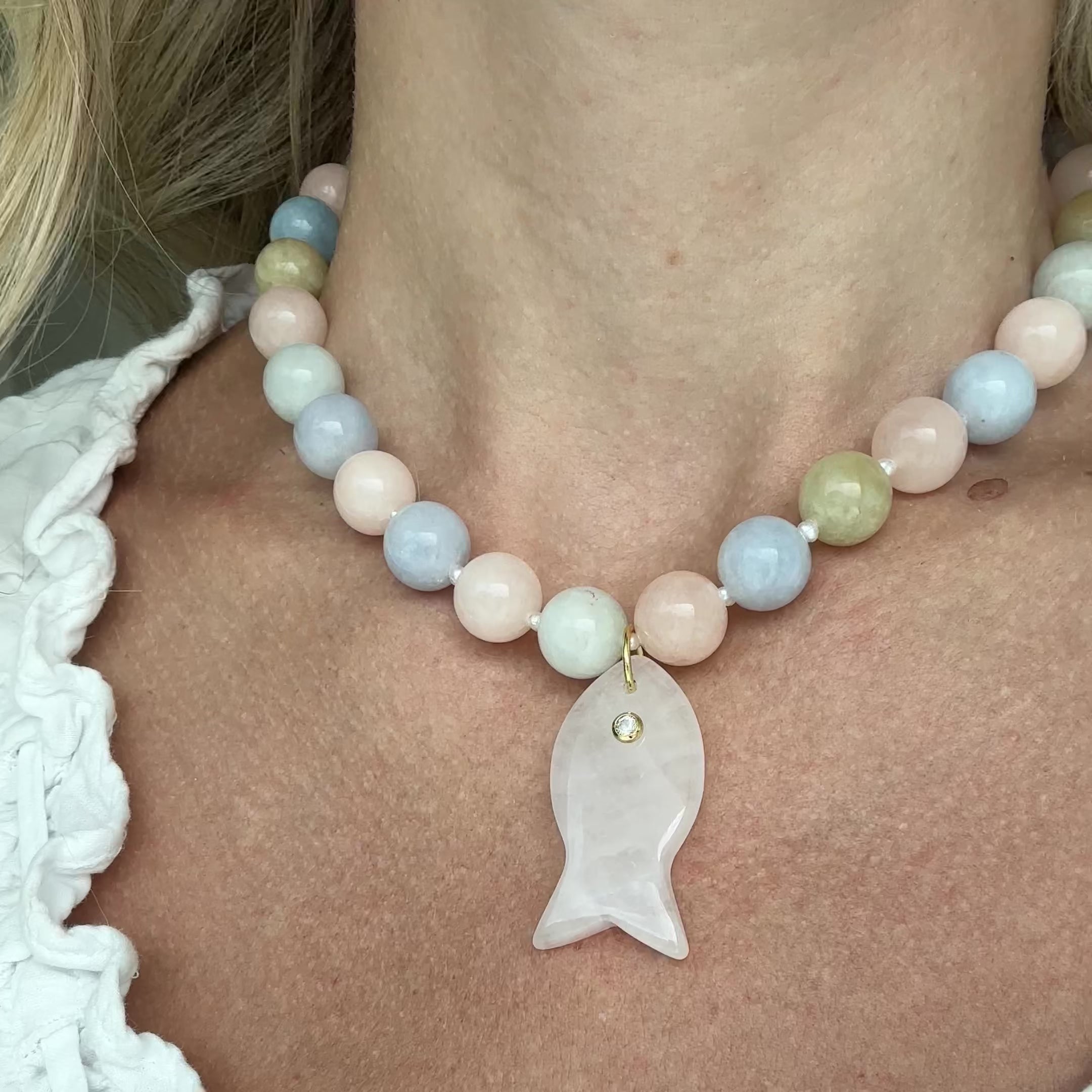 Necklace with pastel beads and a light pink fish pendant worn by a person