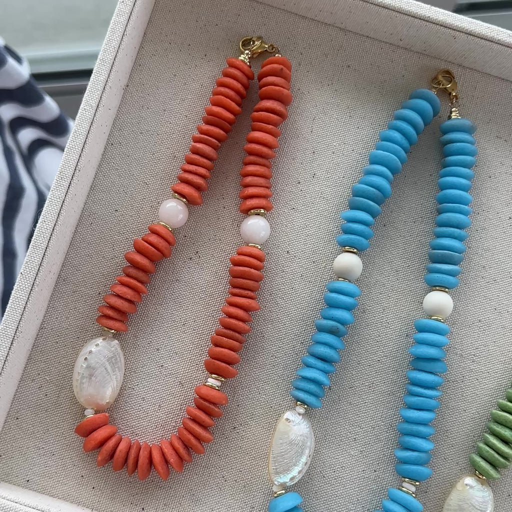 An orange necklace, Blue Necklace and Green Necklace shown on a linen box.