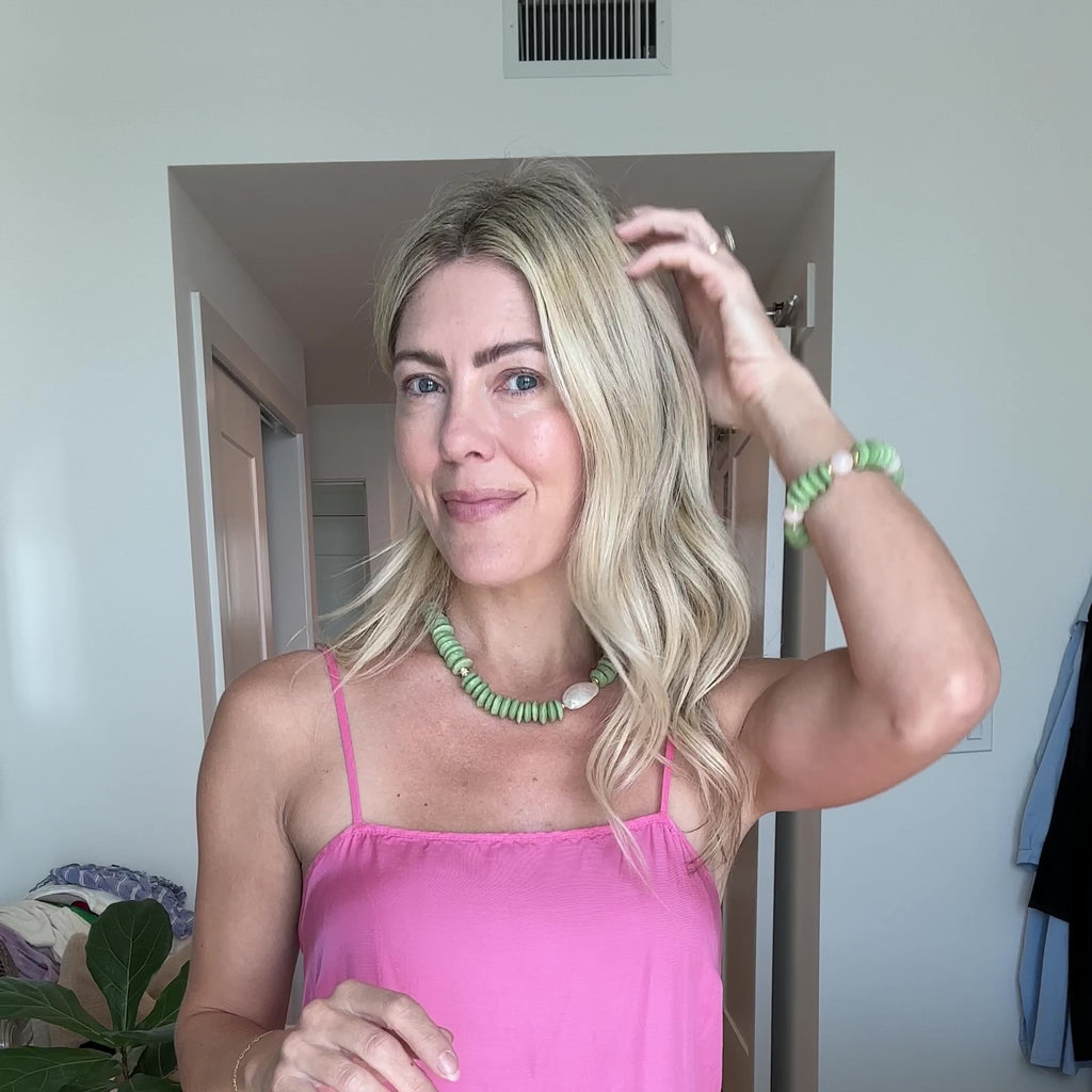 Necklace with green beads and white abalone shell and light pink quartz beads with gold elements on a person wearing a pink dress.