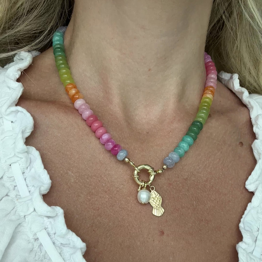 Rainbow gemstone beaded necklace with pearl charm and gold fish charm detail in multicolor tones on a person.