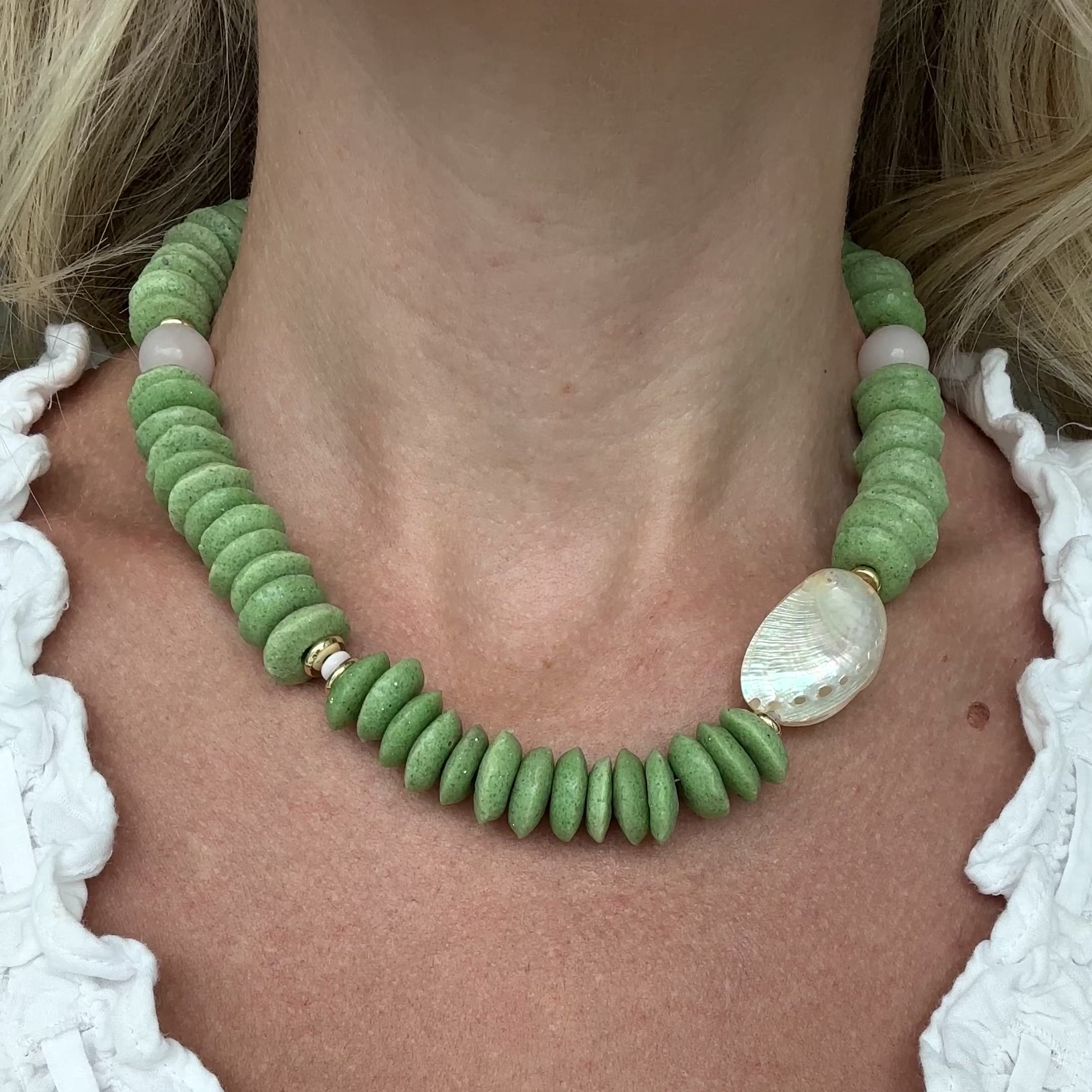 Necklace with green beads and white abalone shell and light pink quartz beads with gold elements on a person.