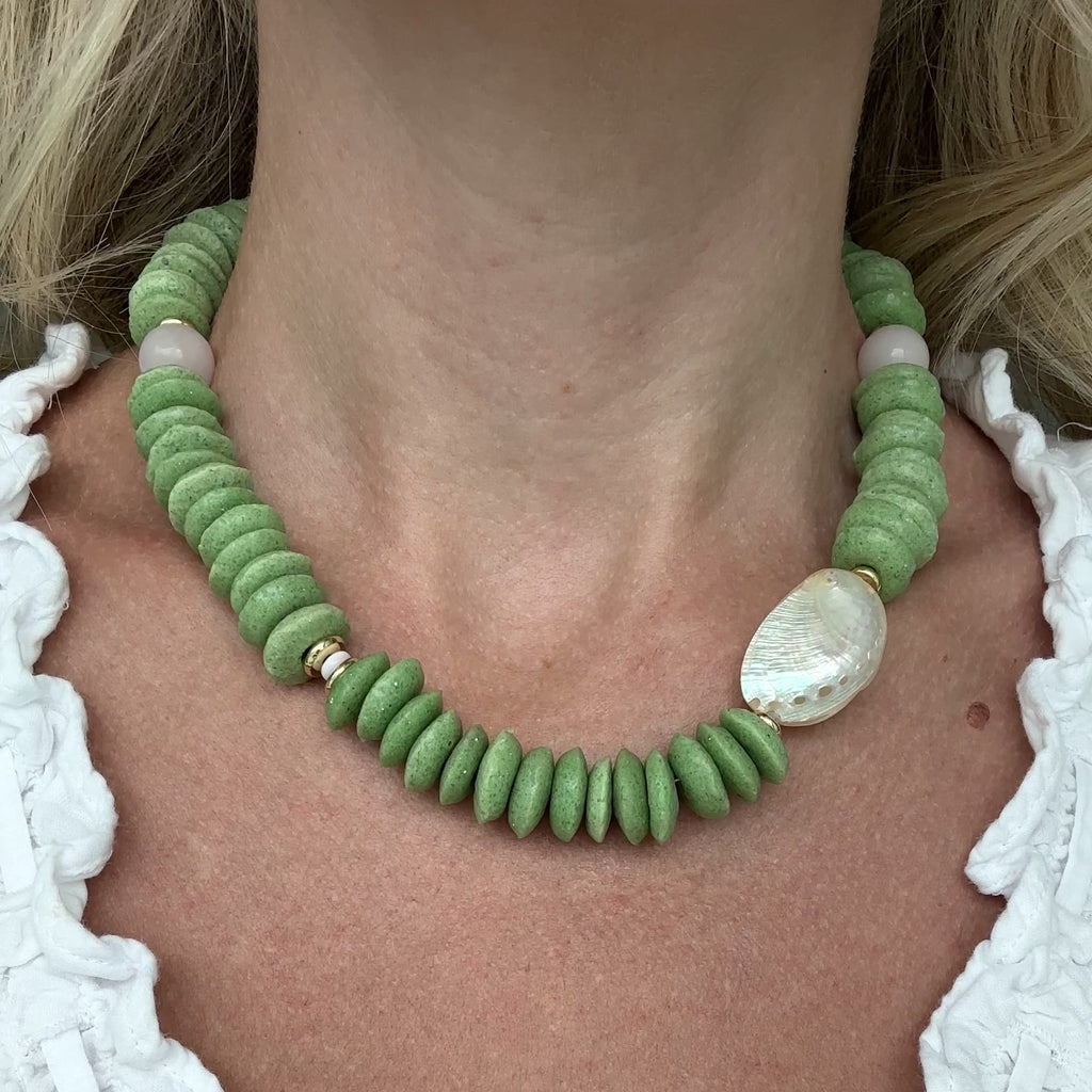 Necklace with green beads and white abalone shell and light pink quartz beads with gold elements on a person.