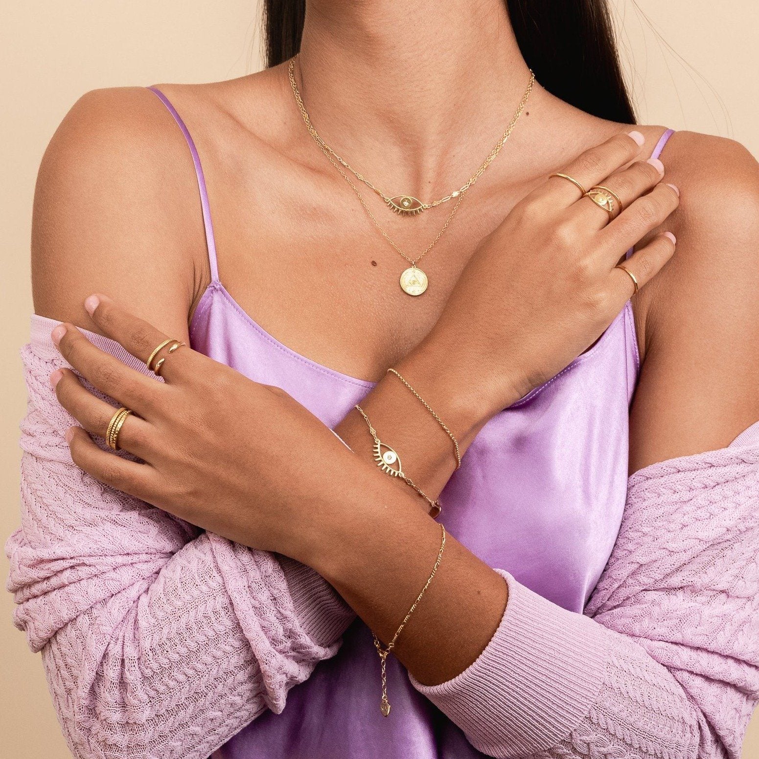 Picture of a model crossing her arms and wearing two dainty gold bracelets on her right wrist, one Evil Eye Bracelet and one Gold Rolo Bracelet, handmade by Katie Dean Jewelry