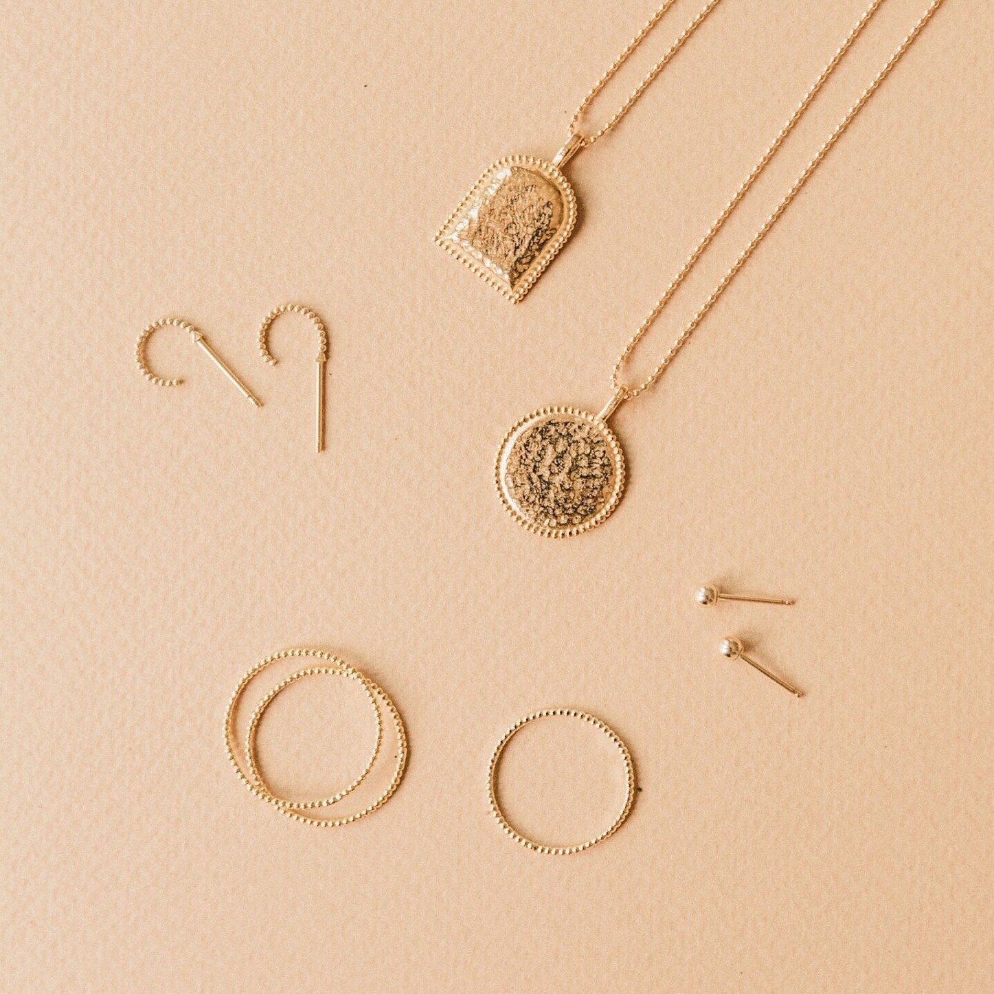 Beaded Coin Necklace, Beaded Arch Necklace, Beaded Rings and Beaded Hoop Earrings laying on a light brown background.