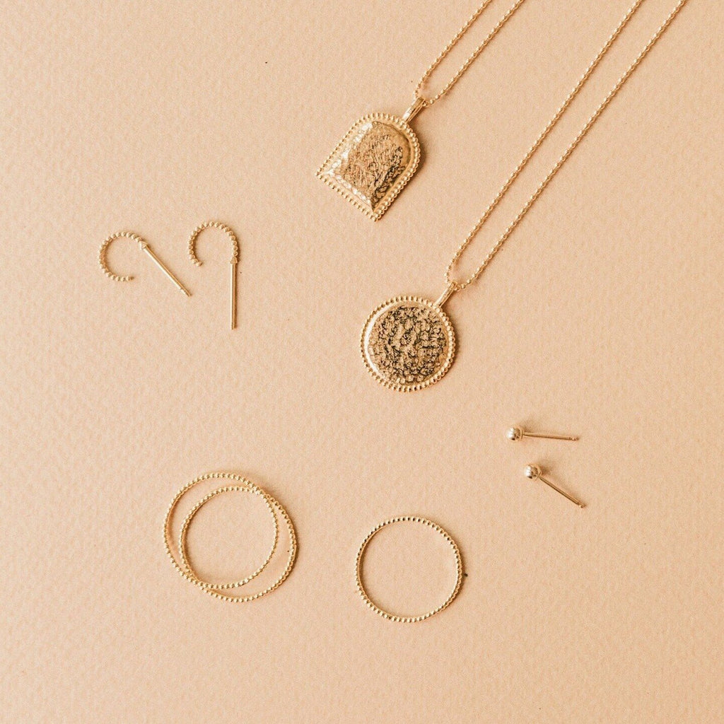 Beaded Coin Necklace, Beaded Arch Necklace, Beaded Rings and Beaded Hoop Earrings laying on a light brown background.