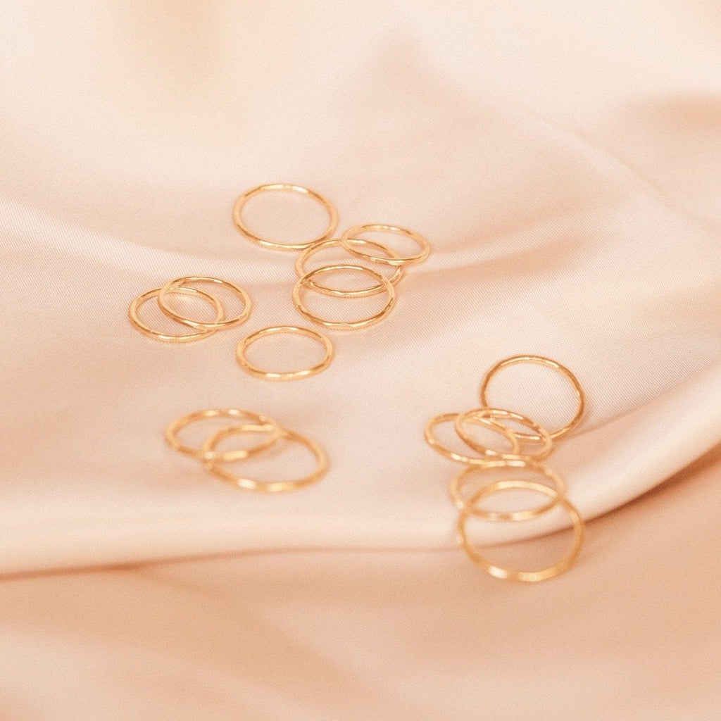 Dainty gold hammered band rings laid out on a piece of pink satin. Handmade by Katie Dean Jewelry in California.