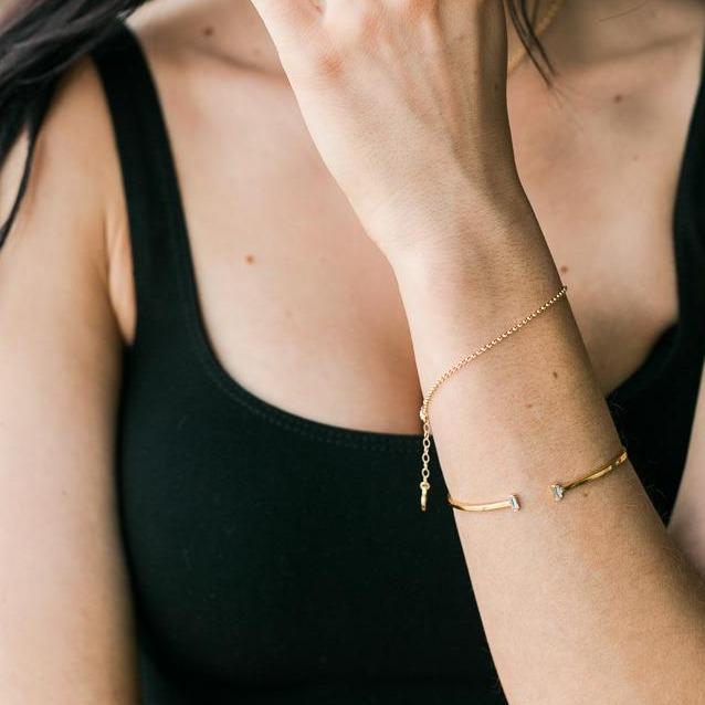 Picture of a model crossing her arm across the frame of the photo and wearing two dainty gold bracelets on her right wrist, one Evil Eye Bracelet and one Gold Rolo Bracelet, handmade by Katie Dean Jewelry