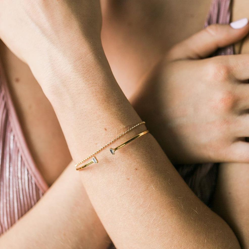 Picture of a model crossing her arms wearing two dainty gold bracelets, one Baguette Cuff and one gold rolo bracelet, both made by Katie Dean Jewelry