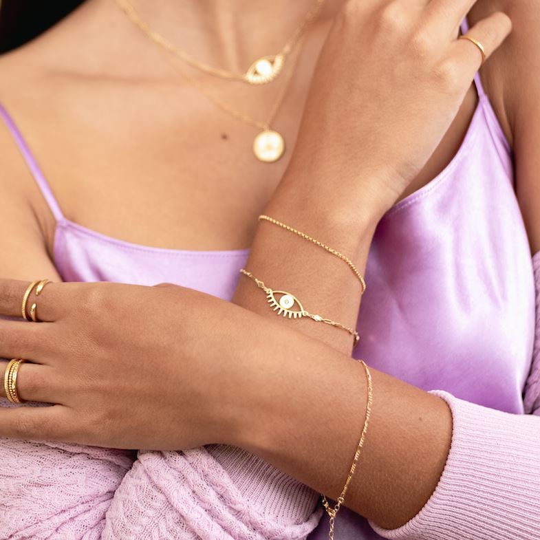 Picture of a model crossing her arms and wearing two dainty gold bracelets on her right wrist, one Evil Eye Bracelet and one Gold Rolo Bracelet, handmade by Katie Dean Jewelry