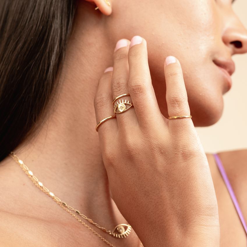 Picture of model with her hand reaching to her chin wearing four dainty gold rings, featuring the Evil Eye Ring Stack made by Katie Dean Jewelry.
