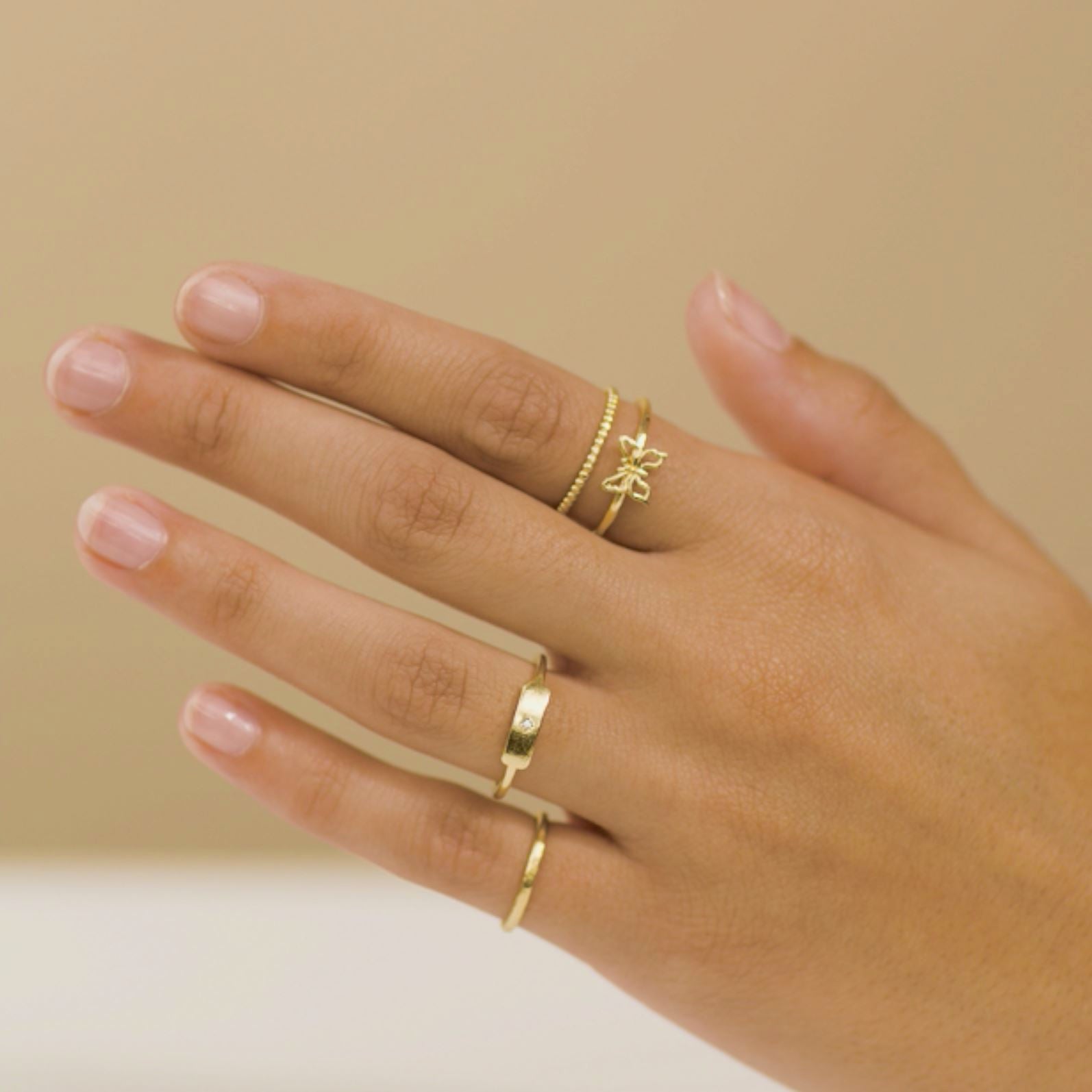 Hand model wearing dainty golden rings, hammered Band ring, Rectangle Ring, Beaded Ring and Butterfly ring, Katie Dean Jewelry