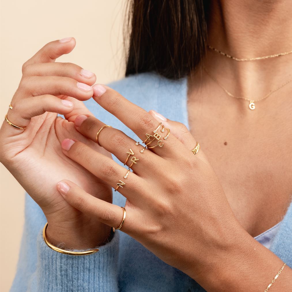 Two hands showing in the center of the image wearing the Initial Rings and Hammered Band Rings made by Katie Dean Jewelry.