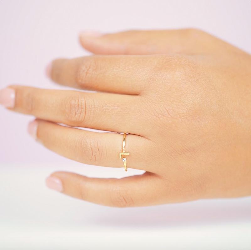 Dainty gold L Initial Ring shown on a hand against a pink background