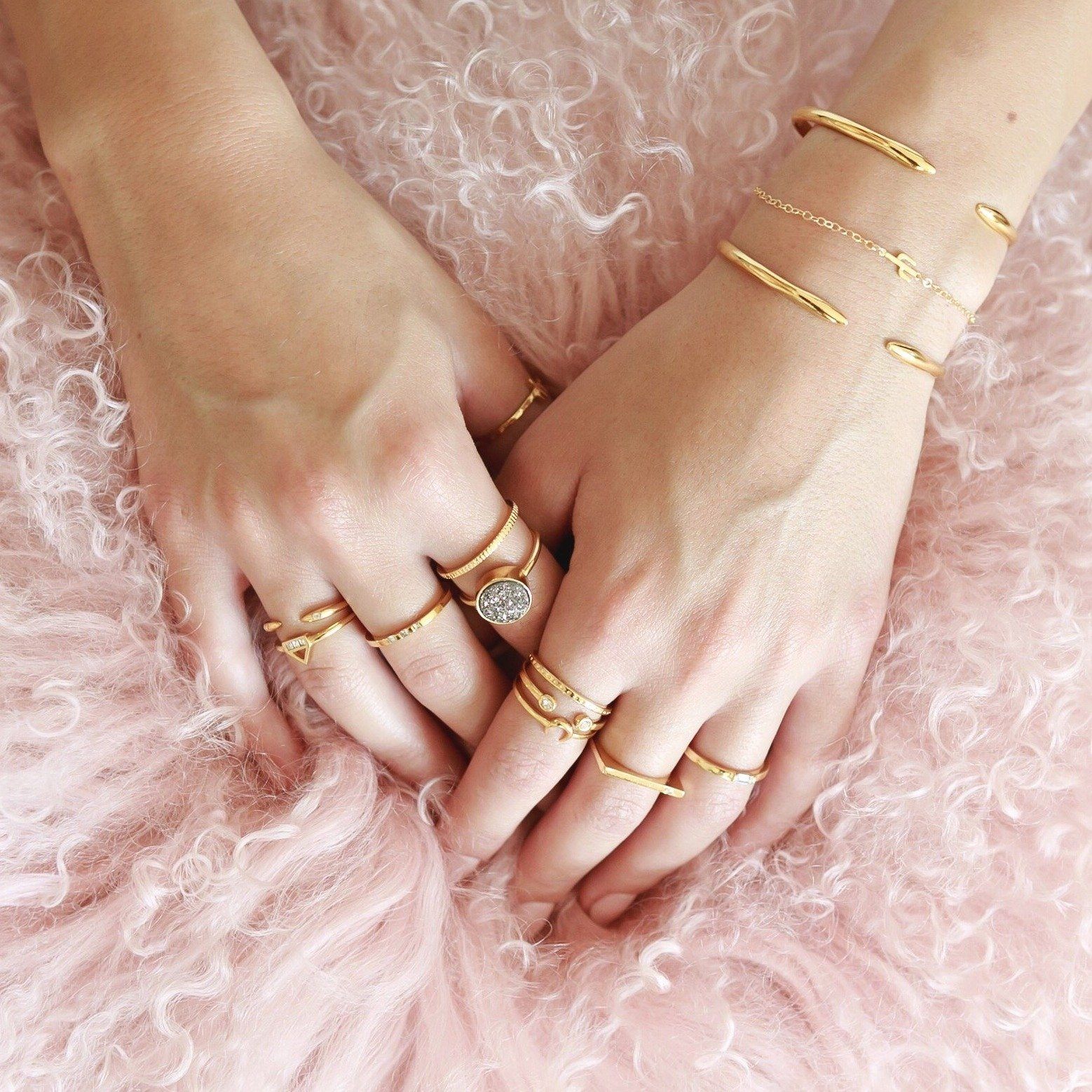 Gold rings layering on the hands of a model on a pink pillow, made by Katie Dean Jewelry
